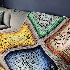 May include: A crocheted blanket with four squares in different colors: green, yellow, blue, and orange. Each square has a lacy pattern in the center.