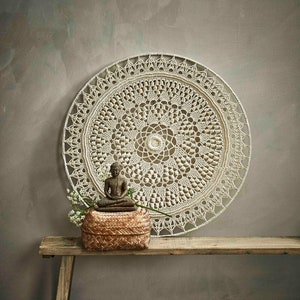 May include: A white crocheted mandala wall hanging with a small Buddha statue and a woven basket on a wooden bench.