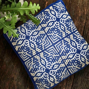 Könnte beinhalten: Ein blaues und weißes gehäkeltes Kissen mit geometrischem Muster. Das Kissen liegt auf einer Holzoberfläche.