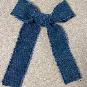 Op de afbeelding: Een blauwe spijkerstrik met gerafelde randen. De strik heeft een diepblauwe kleur en heeft een klassieke vorm. De stof lijkt een medium-gewicht denim te zijn, geschikt voor diverse knutselprojecten of modeaccessoires.