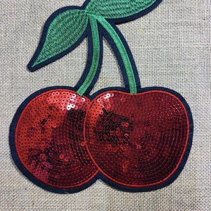 May include: Embroidered cherry patch featuring red sequined cherries, green leaves, and a black outline. Ideal for adding a fruity touch to clothing or accessories.