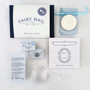 K&ouml;nnte beinhalten: Ein Fairy Mail Set von Little Letter bestehend aus einer dunkelblauen Schachtel, einer silberfarbenen Zahn-M&uuml;nze in einem hellblauen Beutel, einem Miniaturumschlag mit Wachssiegel, einem Brief der Zahnfee, einer Zahnverlust-Tabelle und einer Lupe aus klarem Kunststoff.