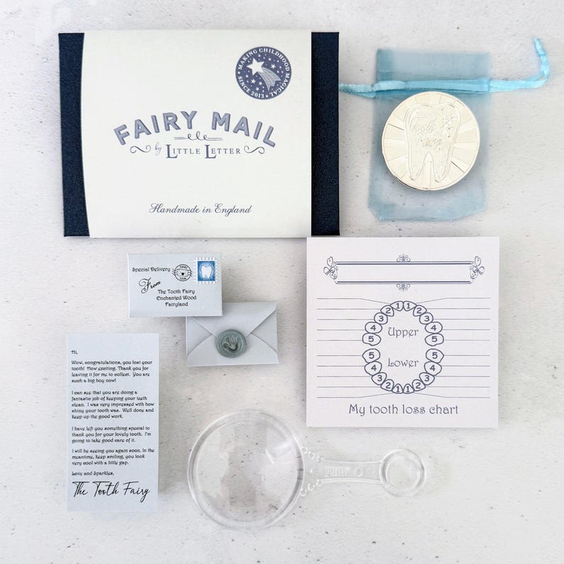 K&ouml;nnte beinhalten: Ein Fairy Mail Set von Little Letter bestehend aus einer dunkelblauen Schachtel, einer silberfarbenen Zahn-M&uuml;nze in einem hellblauen Beutel, einem Miniaturumschlag mit Wachssiegel, einem Brief der Zahnfee, einer Zahnverlust-Tabelle und einer Lupe aus klarem Kunststoff.