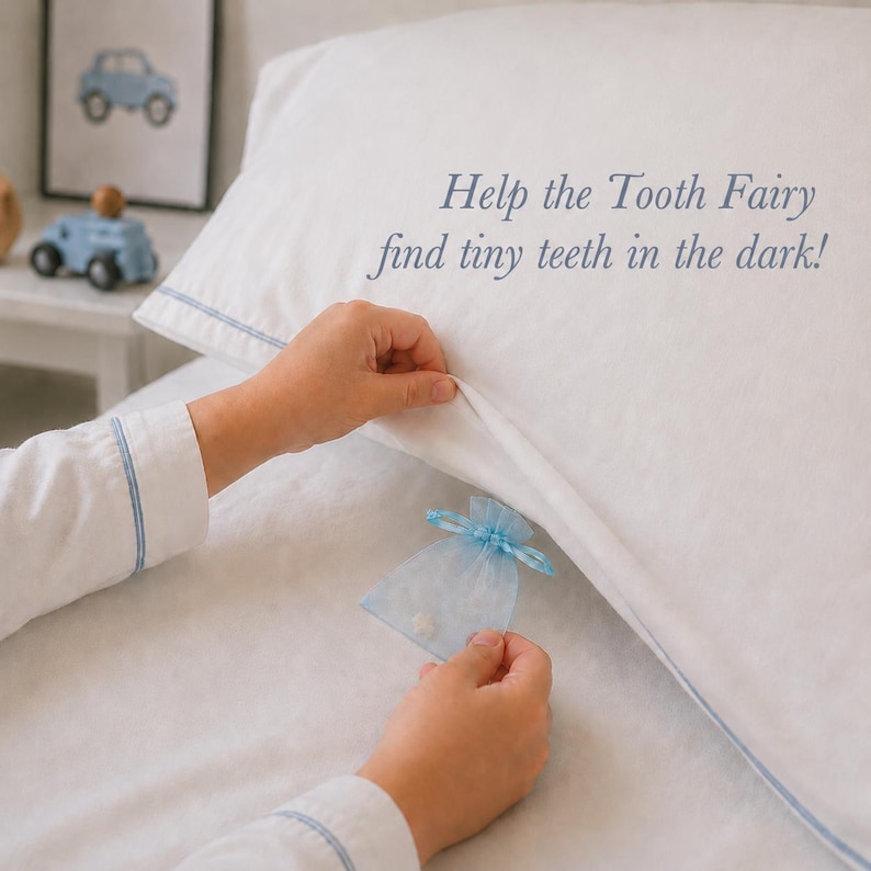 K&ouml;nnte beinhalten: Ein wei&szlig;er Kissenbezug mit blauer Paspelierung und dem gestickten Text Help the Tooth Fairy find tiny teeth in the dark! Ein kleiner, hellblauer Organzabeutel mit Kordelzug wird nahe am Rand des Kissenbezugs aus wei&szlig;em Stoff gehalten.