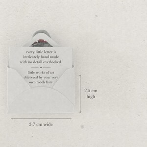 K&ouml;nnte beinhalten: Ein kleiner cremefarbener Umschlag mit einer Karte, auf der steht: every little letter is intricately hand made with no detail overlooked. little works of art delivered by your very own tooth fairy. Der Umschlag ist 3,7 cm breit und 2,5 cm hoch.