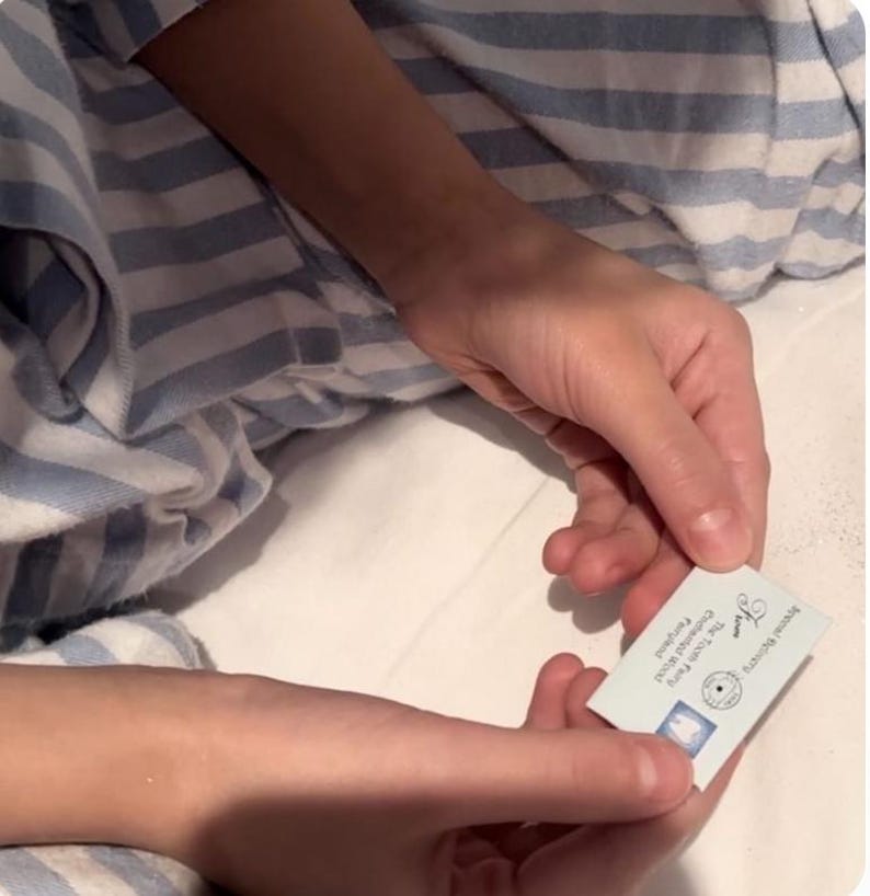 K&ouml;nnte beinhalten: Eine kleine rechteckige hellblaue Karte mit wei&szlig;em Text und einem Zahnsymbol. Die Karte enth&auml;lt den aufgedruckten Text "From The Tooth Fairy" und "Enchanted Tooth Fairy Land" sowie ein kreisf&ouml;rmiges Stempeldesign und eine kleine blaue Zahngrafik.