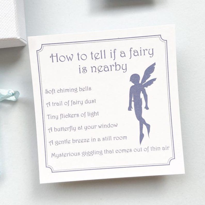 K&ouml;nnte beinhalten: Eine quadratische wei&szlig;e Karte mit dekorativem Rand, die den violetten Text How to tell if a fairy is nearby und eine Liste von sechs Anzeichen wie sanfte Glockenkl&auml;nge und Feenstaub sowie eine violette Silhouette einer gefl&uuml;gelten Fee zeigt.