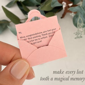 以下が含まれることがあります： 淡いピンク色のミニチュア紙封筒。中には黒い文字で「Hi, Wow, congratulations, you lost your tooth! How exciting. Thank you for saving it for me to collect. You are a big girl now!」と印刷された小さなメモが入っています。