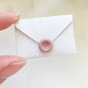 Op de afbeelding: Een witte envelop met een roze hartvormige waszegel. De envelop heeft een delicaat bloemenpatroon.