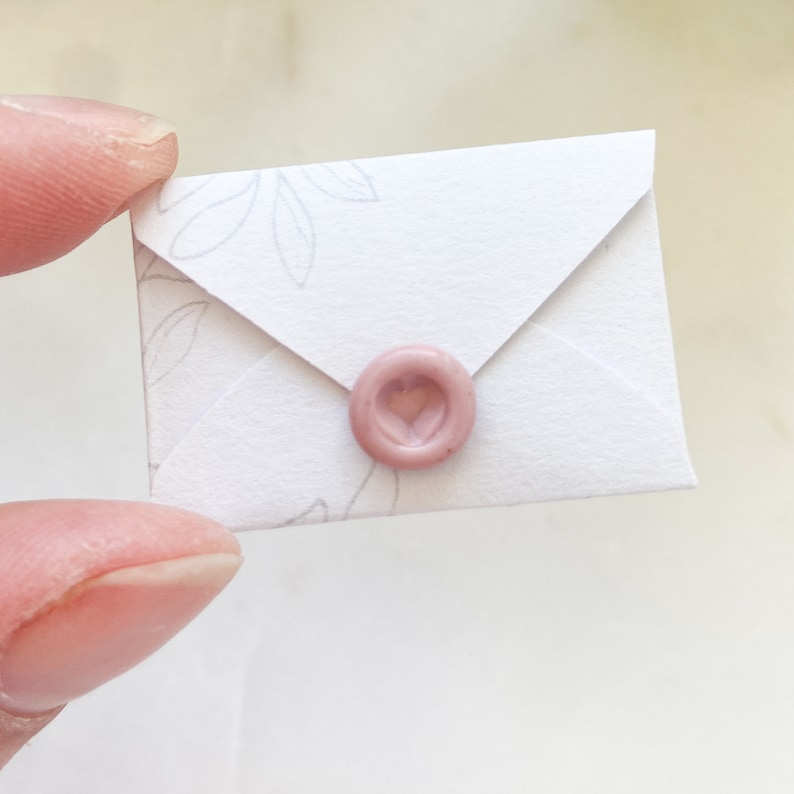 Op de afbeelding: Een witte envelop met een roze hartvormige waszegel. De envelop heeft een delicaat bloemenpatroon.