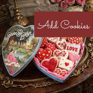 May include: A heart-shaped tin box filled with decorated cookies. The cookies are in the shape of hearts and other shapes, with red, white, and pink icing. The box is open, revealing the treats inside. The text "Add Cookies" is displayed.