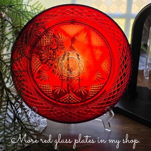 May include: A circular red glass plate featuring a pressed diamond pattern around the rim and a central starburst design with radiating leaf-like motifs. The plate is displayed on a clear stand and includes the text More red glass plates in my shop.