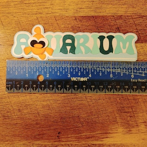 May include: A light blue and green paper cutout of the word "AQUARIUM" with a small orange fish cutout in the "A".