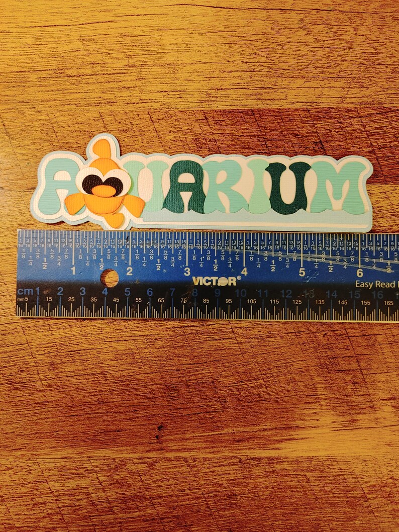 May include: A light blue and green paper cutout of the word "AQUARIUM" with a small orange fish cutout in the "A".