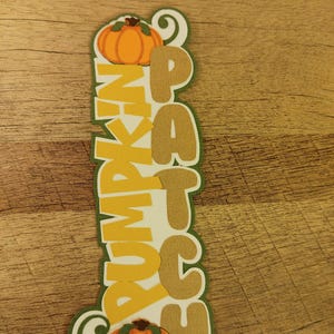 May include: A white background with a green, yellow, and orange pumpkin patch sign. The sign says "Patch" in brown letters and "Pumpkin" in yellow letters.