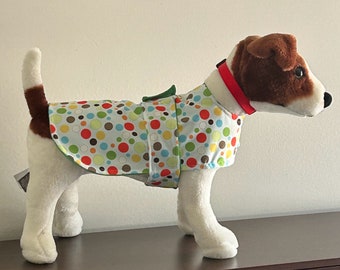 May include: A dog coat with a colorful polka dot pattern in red, orange, yellow, green, and brown on a light blue background. The coat has a green trim and is worn by a stuffed dog with a red collar.