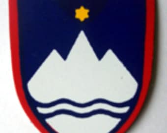 May include: A blue and red shield with a white mountain range and a wavy line at the bottom. Three yellow stars are at the top of the shield.