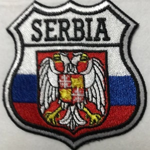 Pode incluir: Etiqueta bordada com a palavra "SERBIA" em letras pretas sobre fundo branco. A etiqueta apresenta uma bandeira vermelha, branca e azul com uma águia branca e um escudo amarelo com uma cruz vermelha.