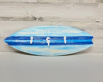 May include: A blue and white surfboard-shaped key holder with three hooks. The hooks are shaped like a seahorse and two simple hooks.