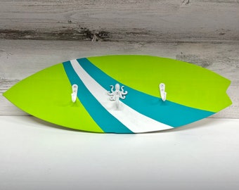 May include: A green and blue surfboard-shaped wall hook with three white hooks and an octopus design.