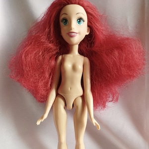 May include: A nude plastic doll with long, red, wavy hair. The doll has blue eyes and a painted smile.