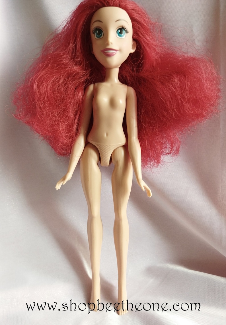 May include: A nude plastic doll with long, red, wavy hair. The doll has blue eyes and a painted smile.