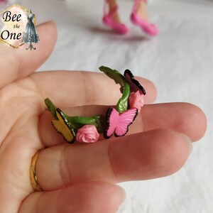 以下が含まれることがあります： ピンクの花と蝶がついた緑色のプラスチック製のヘッドバンド。ヘッドバンドはピンクと黄色の蝶とピンクの花で飾られています。