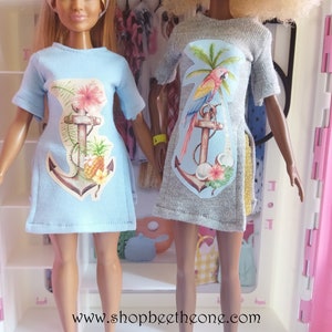 May include: Two dolls wearing blue and gray t-shirts with a tropical anchor design. The shirts feature a parrot, palm tree, pineapple, and flowers. The text "www.shopbeethetone.com" is visible at the bottom of the image.