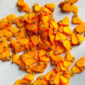 Peut inclure: Un grand tas de décorations plates en résine orange et jaune en forme de tranche de mangue avec un détail d'œil noir.