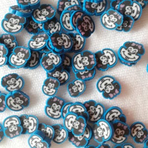 May include: A collection of small, round, blue and white polymer clay beads. Each bead features a cartoon character face with a black outline, white face, and pink bow. The website address "www.shopbeetheone.com" is visible at the bottom.