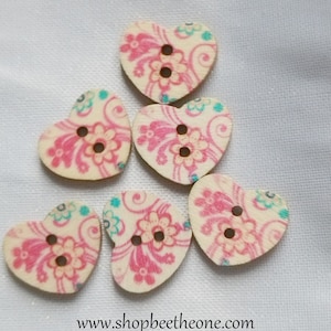 Peut inclure: Six boutons en bois en forme de cœur avec un motif floral rose et blanc. Les boutons ont deux trous chacun.