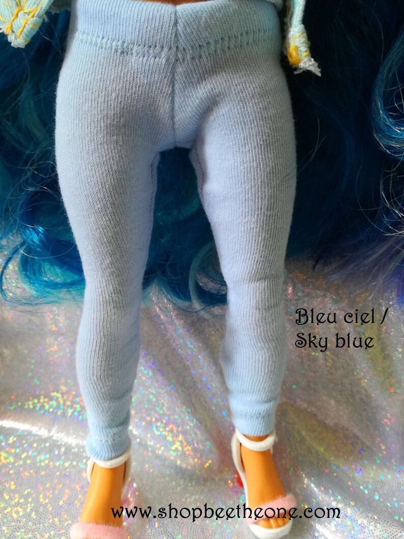 May include: Light blue leggings for a doll. The leggings are made of a soft, stretchy fabric. The text "Bleu ciel / Sky blue" is written on the image.