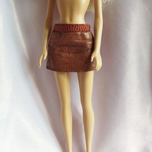 Peut inclure: Une mini-jupe en similicuir marron avec une ceinture tressée rouge et orange.