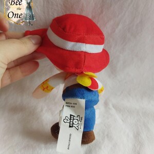 K&ouml;nnte beinhalten: Rotes und wei&szlig;es Pl&uuml;schtier von Woody aus Toy Story 4. Woody tr&auml;gt seinen charakteristischen Cowboyhut und seine Weste. Das Spielzeug ist etwa 15 cm gro&szlig;. Das Etikett auf dem Spielzeug lautet "Disney Pixar Toy Story 4".