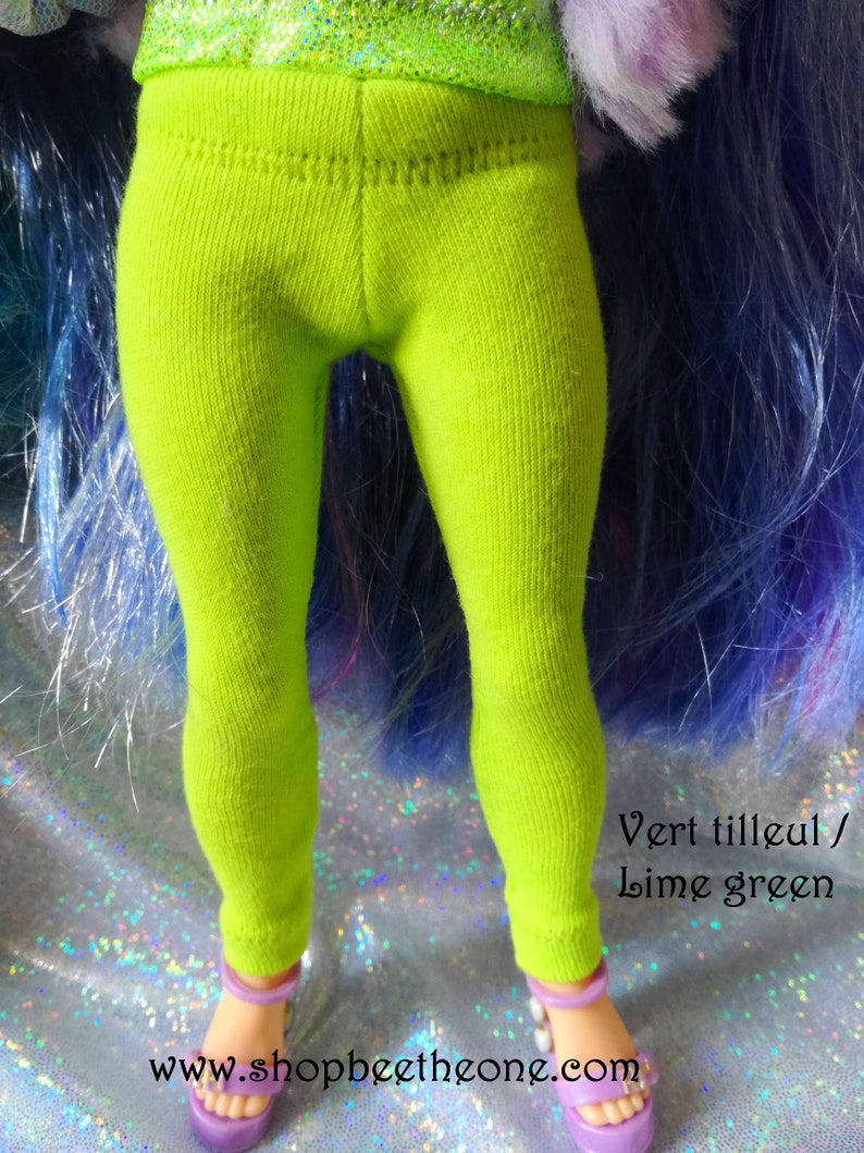 May include: Lime green leggings for a doll. The leggings are made of a soft, stretchy fabric and have a ribbed texture. The text "Vert tilleul / Lime green" is visible at the bottom of the image.