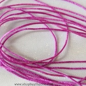 Peut inclure: Gros plan sur un tas de cordon de satin rose vif. Le cordon est finement tissé et légèrement brillant. Le fond est un tissu clair et texturé. L'adresse du site Web www.shopbeethezone.com est visible en bas.