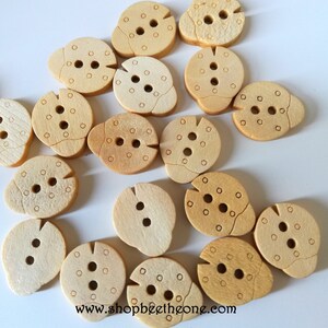 May include: A collection of 15 wooden buttons in a light brown colour. Each button has a unique shape and features a two-hole design with a circle pattern.