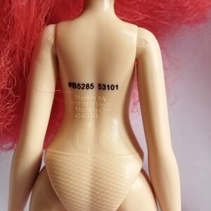 May include: A pink haired doll with a tan body and a white swimsuit. The doll has a sticker on its back with the text #B5285 53101, Hasbro SA, &copy; 2015 Hasbro, Made in China, C-03 G.