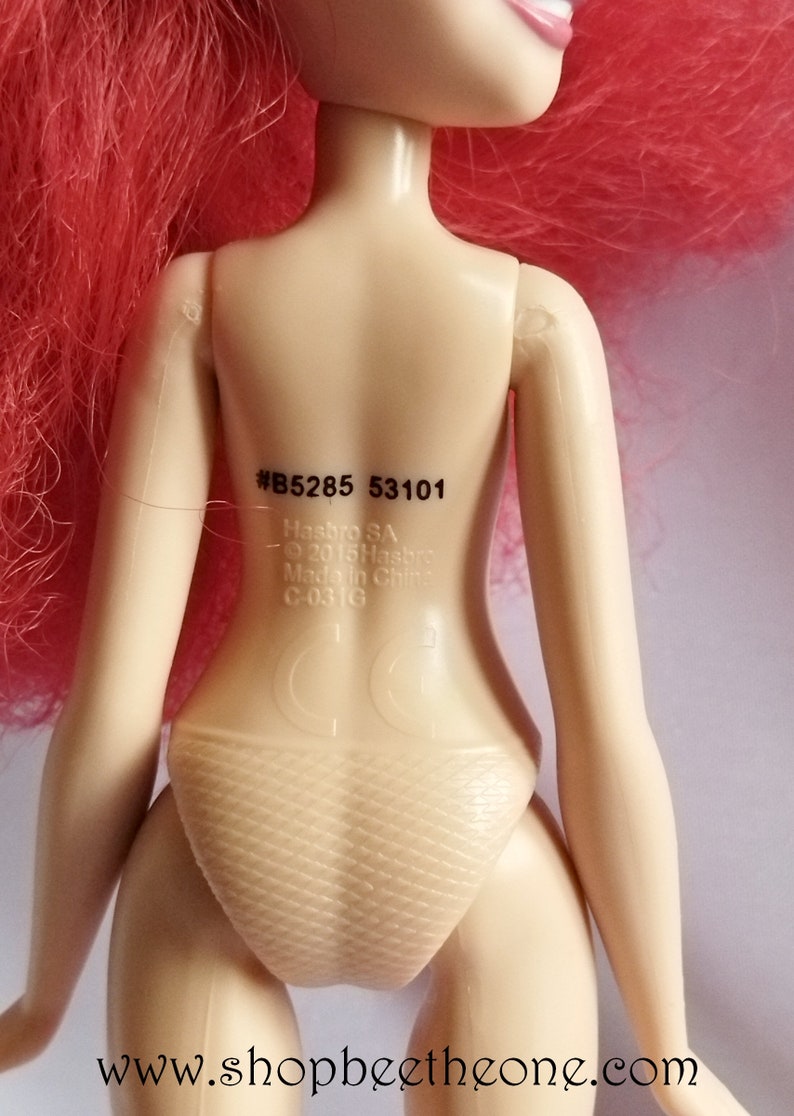 May include: A pink haired doll with a tan body and a white swimsuit. The doll has a sticker on its back with the text #B5285 53101, Hasbro SA, &copy; 2015 Hasbro, Made in China, C-03 G.