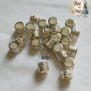 Op de afbeelding: Een groep zilverkleurige metalen haar kralen met een decoratief swirl-ontwerp. De kralen zijn verspreid over een wit stofoppervlak. De tekst "x2p" is zichtbaar in de afbeelding.