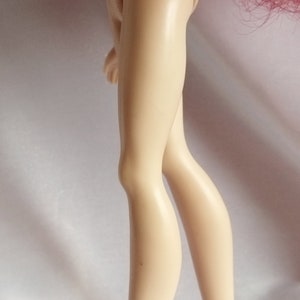 May include: Close-up of a doll's legs, showing the lower legs and feet. The doll has a light skin tone and is wearing no shoes.