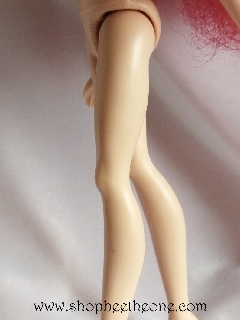 May include: Close-up of a doll's legs, showing the lower legs and feet. The doll has a light skin tone and is wearing no shoes.