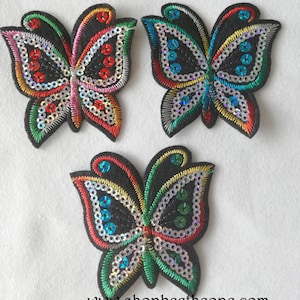 Peut inclure: Trois appliques en feutre noir en forme de papillon avec des paillettes colorées. Les papillons ont des paillettes rouges, vertes, bleues et argentées.