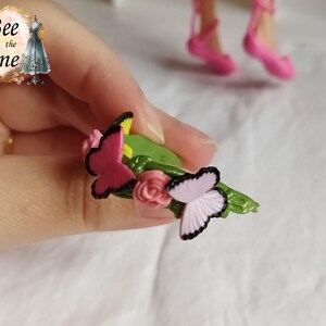 以下が含まれることがあります： ピンクと紫の蝶がついた緑色のプラスチックの花冠。花冠は緑色の土台にピンクと黄色の花が飾られています。