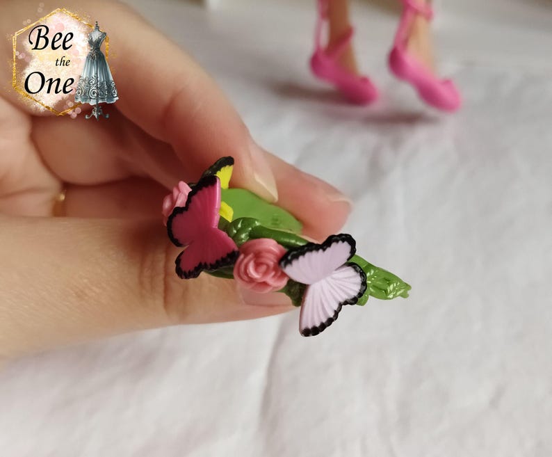 以下が含まれることがあります： ピンクと紫の蝶がついた緑色のプラスチックの花冠。花冠は緑色の土台にピンクと黄色の花が飾られています。
