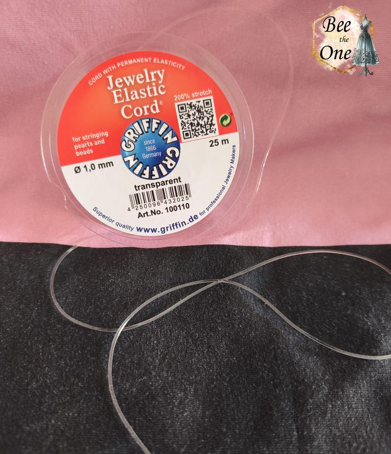 Op de afbeelding: Een spoel Griffin sieradenelastiek met een transparante afwerking. Het etiket geeft een diameter van 1,0 mm, een lengte van 25 m en 200% rek aan. De spoel is voorzien van een QR-code, een streepjescode en de tekst Jewelry Elastic Cord.