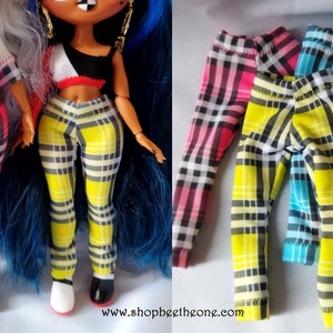 May include: Three pairs of plaid leggings for dolls. The leggings are yellow and black with pink, blue, and turquoise accents. The leggings are folded and stacked on top of each other.