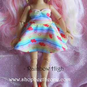 Puede incluir: Un vestido a rayas arcoíris con corazones rojos para una muñeca. El vestido tiene un escote de corazón y una falda completa. La muñeca tiene el pelo largo, rosa y blanco.