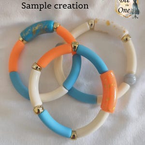 Op de afbeelding: Drie elastische armbanden met cilindrische kralen in oranje, lichtblauw en cr&egrave;me, afgewisseld met goudkleurige tussenstukjes. Sommige kralen hebben gouden spikkels of een marmerpatroon. Tekst bovenaan: Exemple de r&eacute;alisation / Sample creation Bee the One.