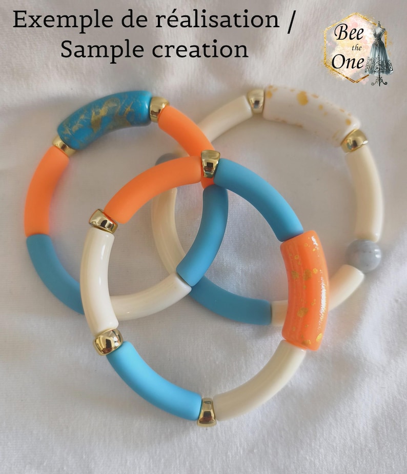Op de afbeelding: Drie elastische armbanden met cilindrische kralen in oranje, lichtblauw en cr&egrave;me, afgewisseld met goudkleurige tussenstukjes. Sommige kralen hebben gouden spikkels of een marmerpatroon. Tekst bovenaan: Exemple de r&eacute;alisation / Sample creation Bee the One.